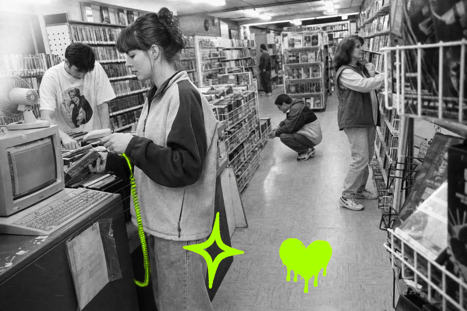 Wide black-and-white point-and-shoot photograph inside a 1997 neighborhood video rental store. A young woman in a zip fleece scans returned VHS tapes at a beige CRT terminal in the foreground while a coworker sorts clamshell cases behind her; two customers browse shelves at mid-distance and a fifth figure disappears toward the back. The coiled barcode-scanner cord glows with a translucent acid-green (#A8FF00) highlighter wash, its ridged texture visible through the color. Direct flash, open shadows, fine film grain.